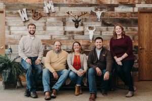 The Wright & Moore team seated in front of a reclaimed wood wall